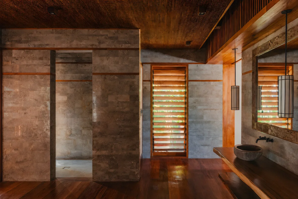 Nihi Rote bathroom: grey stone cladding with timber inlay lines, louvred window and hardwood floor, all aligned to one grid.